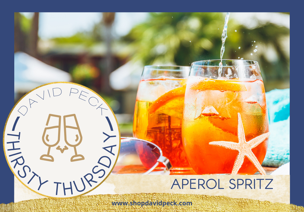 Thirsty Thursday. Aperol Spritz in a stemless wine glass sitting next to sunglasses, starfish, and blue towel.