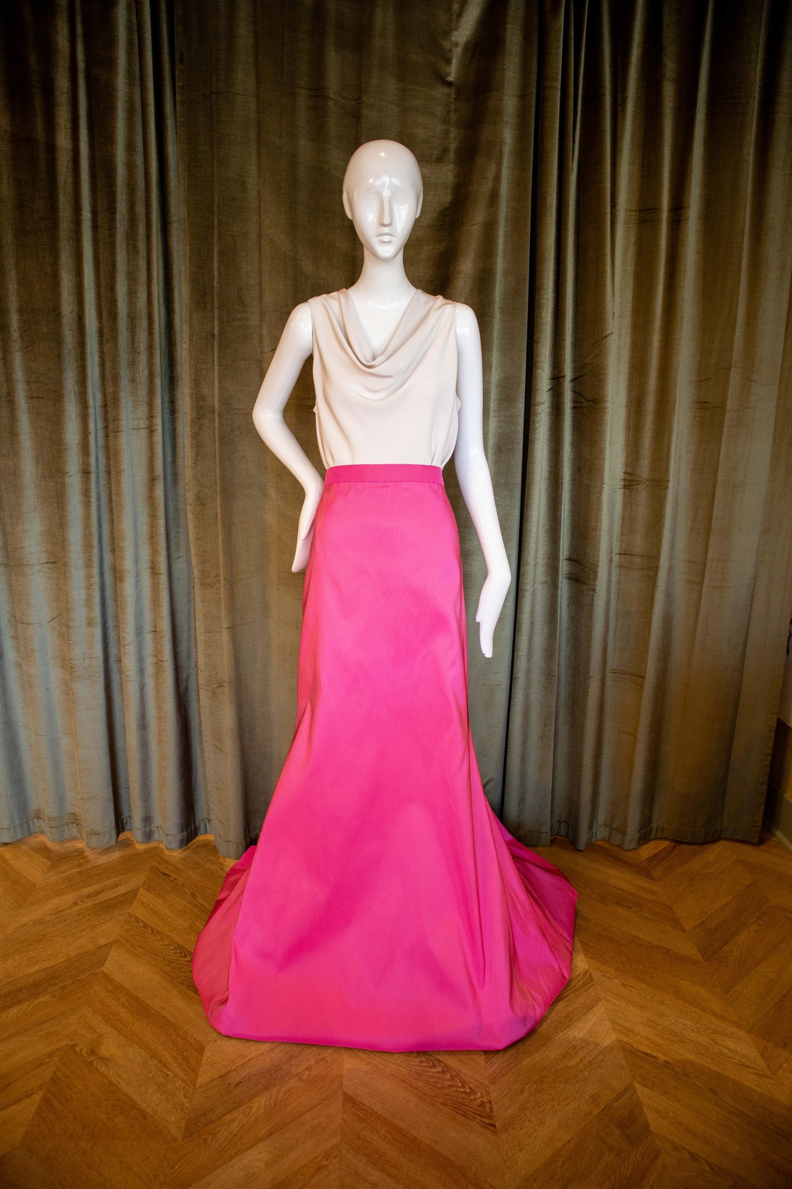 A mannequin displaying a pink silk faille skirt with a tailored fit and a dramatic sweep train. Designed by David Peck