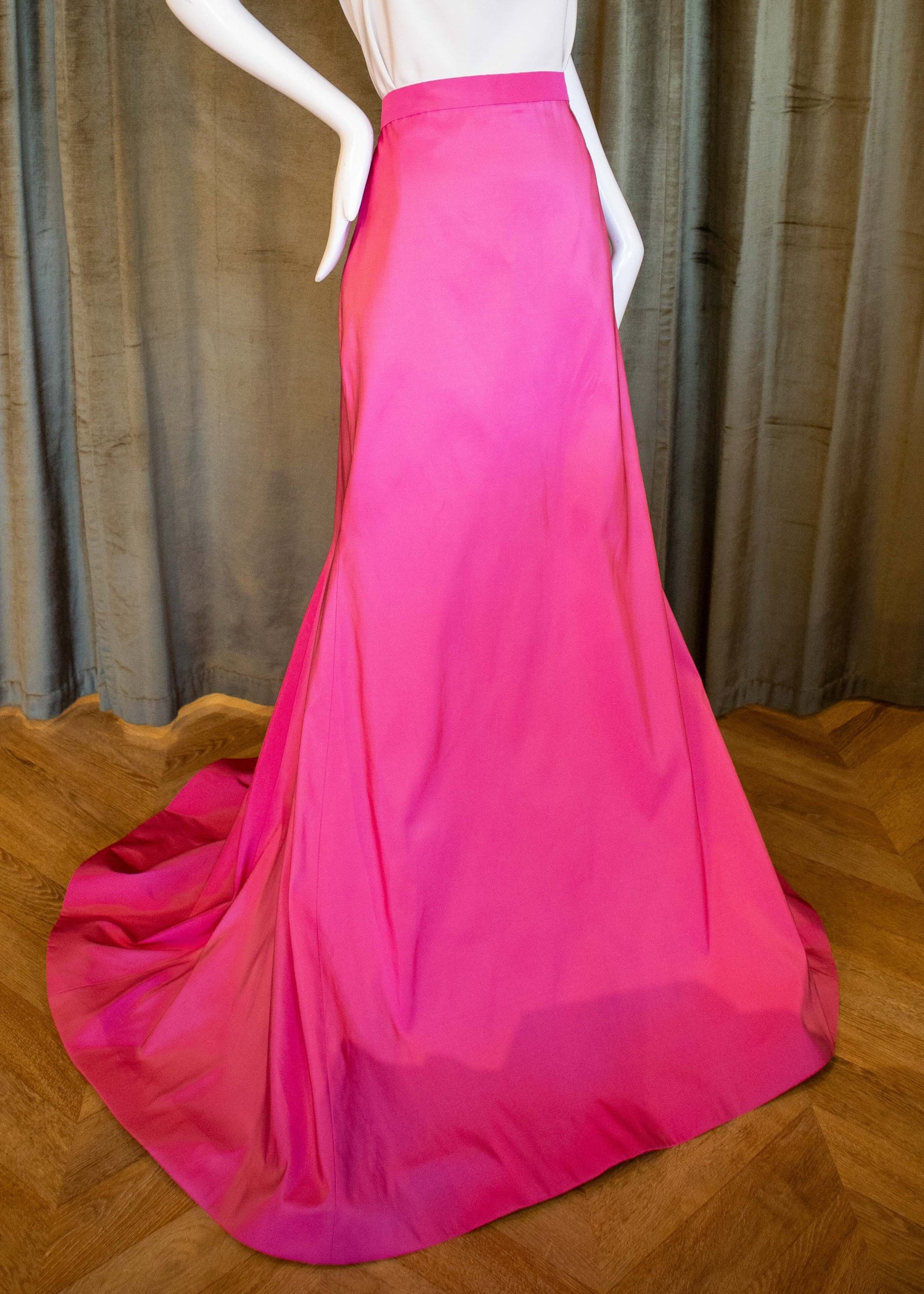 A mannequin displaying a pink silk faille skirt with a tailored fit and a dramatic sweep train. Designed by David Peck