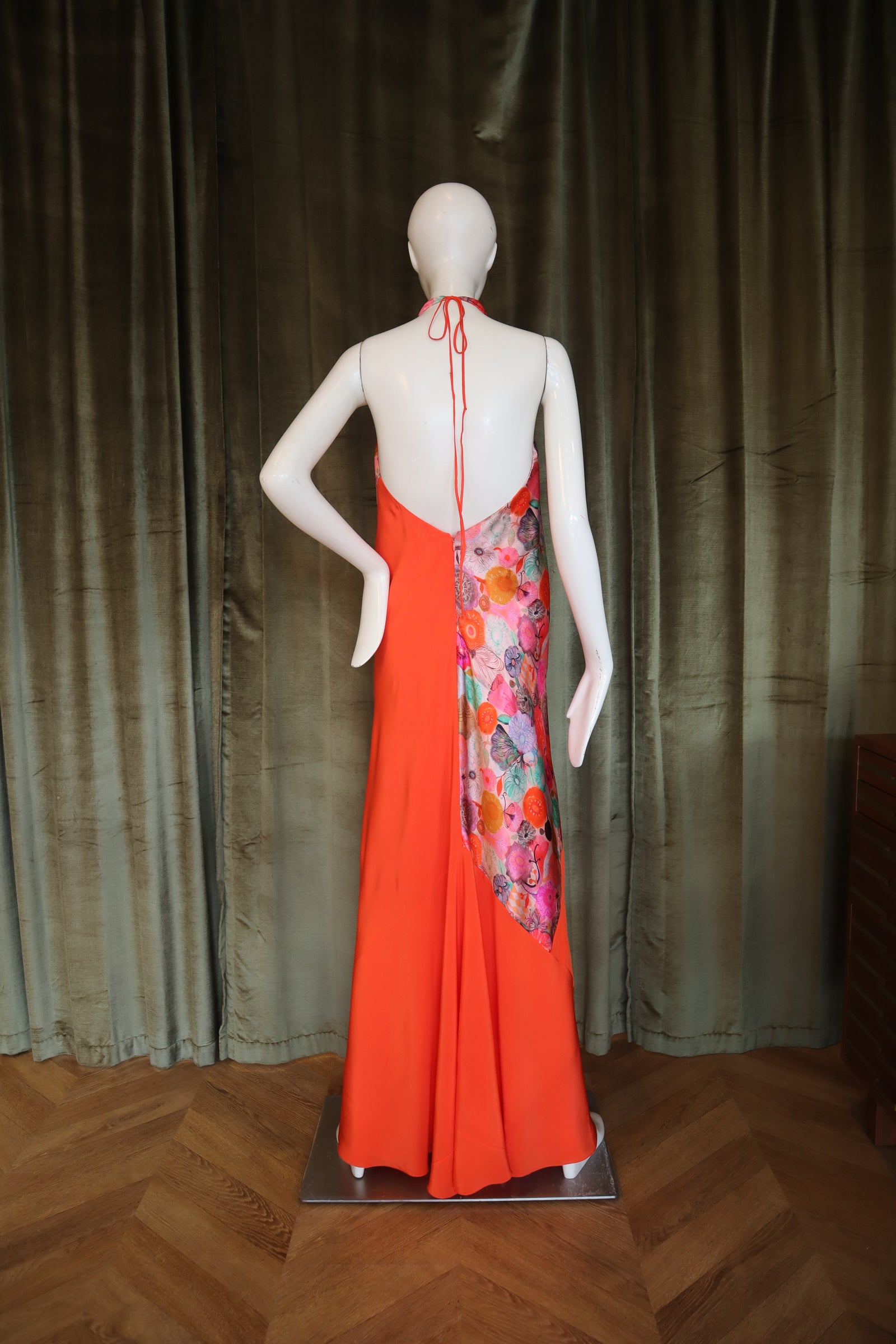 Mannequin wearing a colorful floral dress with an orange skirt on a wooden floor.