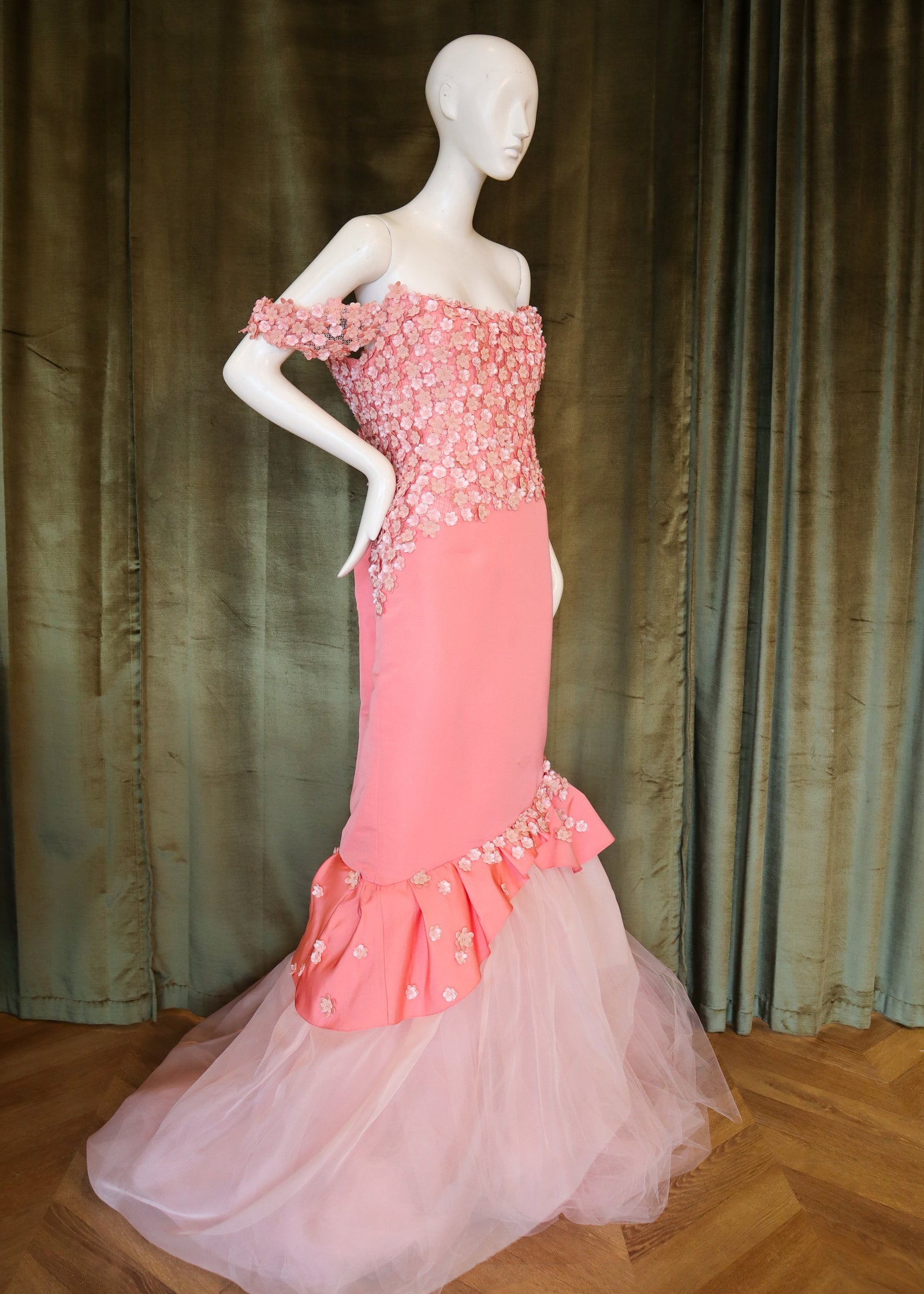 Mannequin wearing a pink evening gown with a textured bodice against a green curtain.