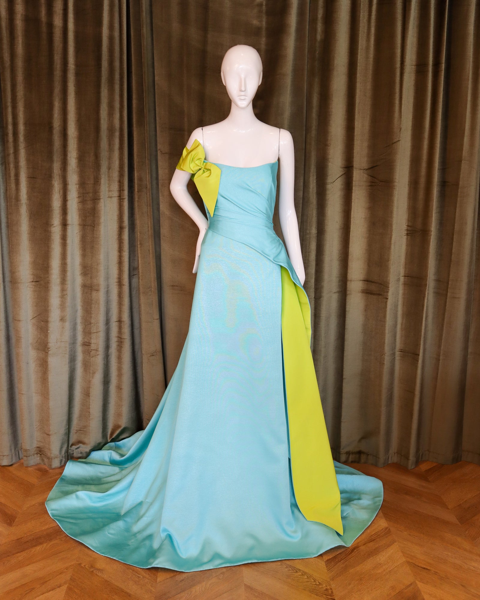 Mannequin wearing a turquoise and green evening gown against a brown curtain background