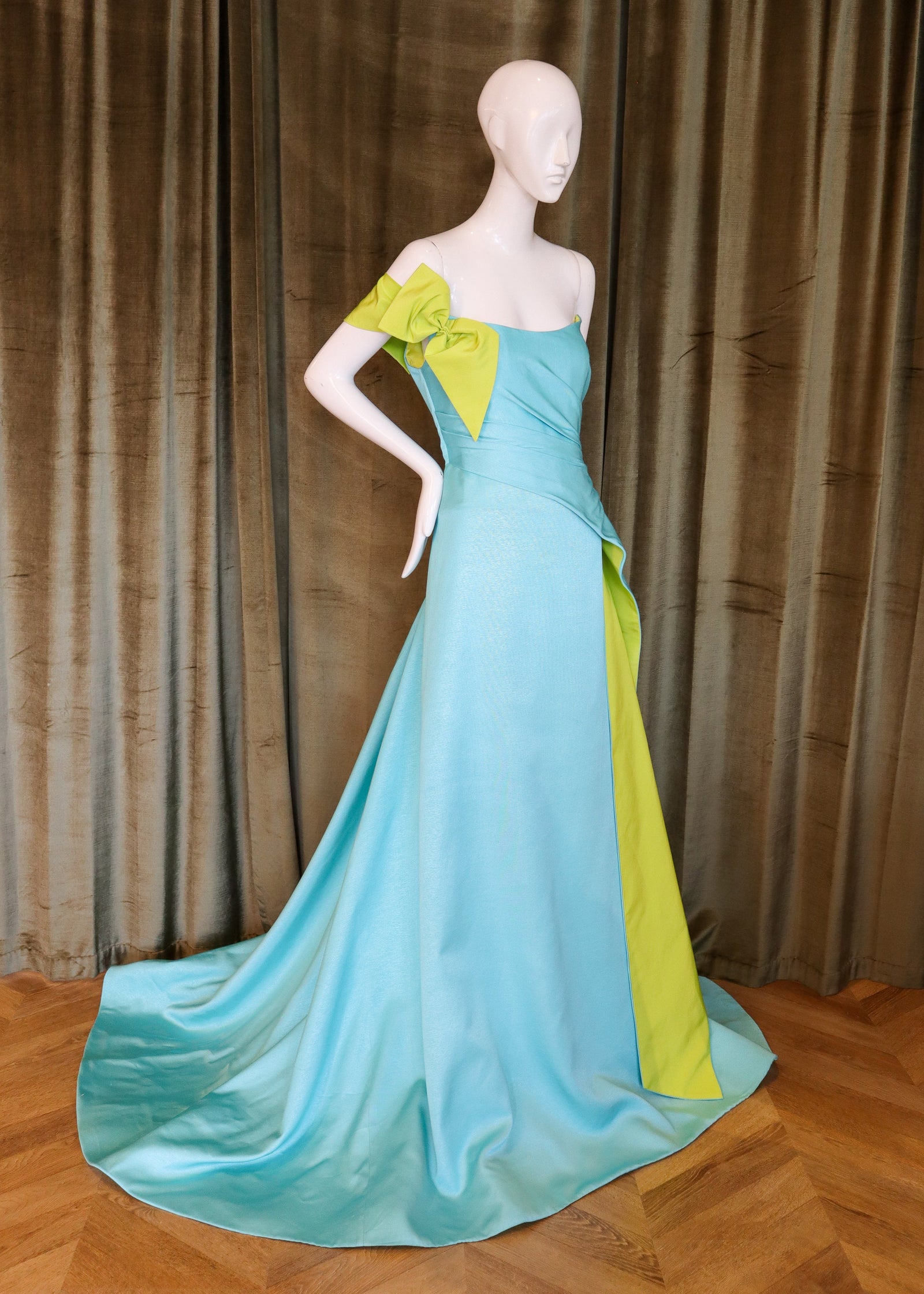 Mannequin wearing a turquoise and green evening gown against a brown curtain background