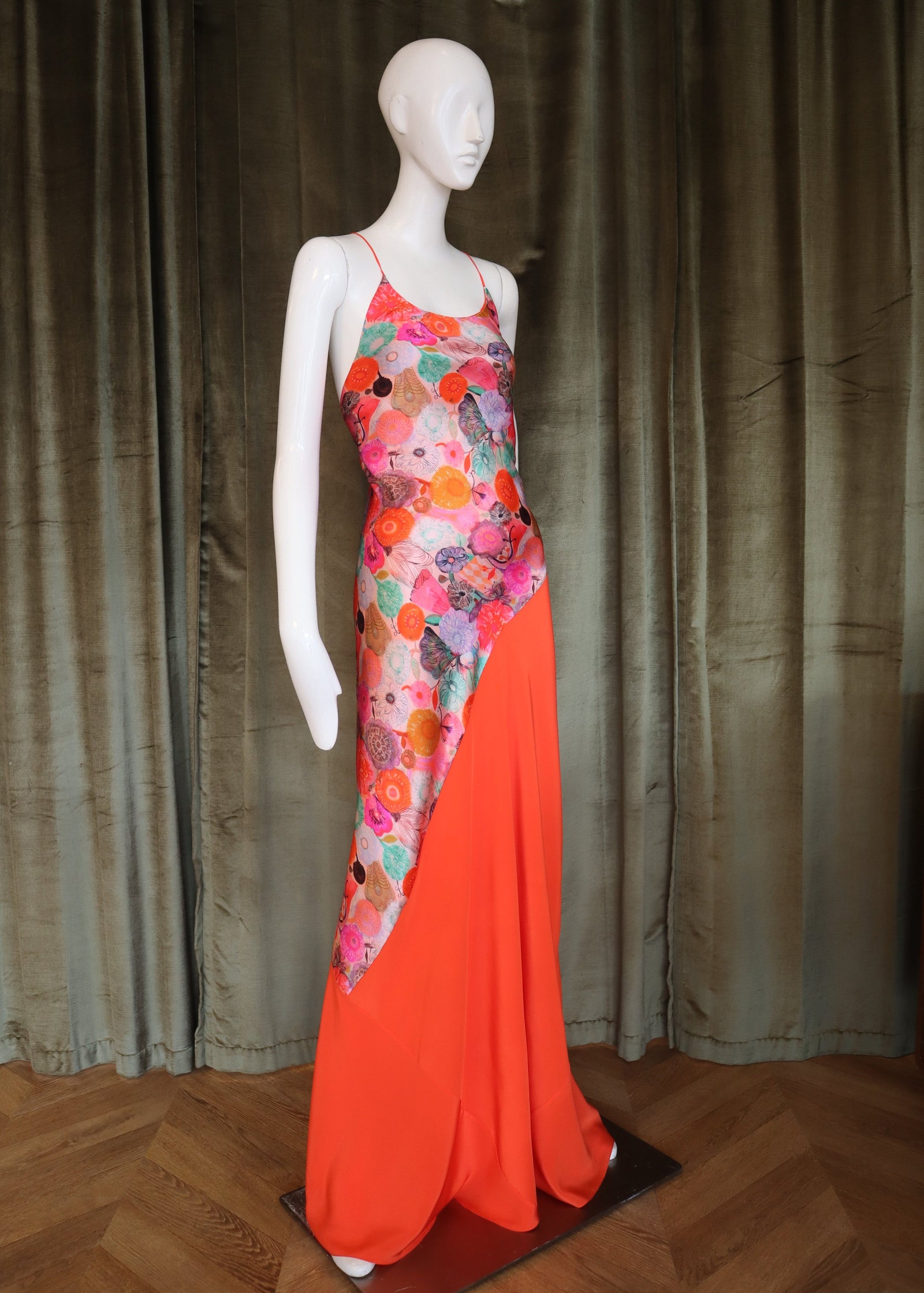 Mannequin wearing a colorful floral dress with an orange skirt on a wooden floor.