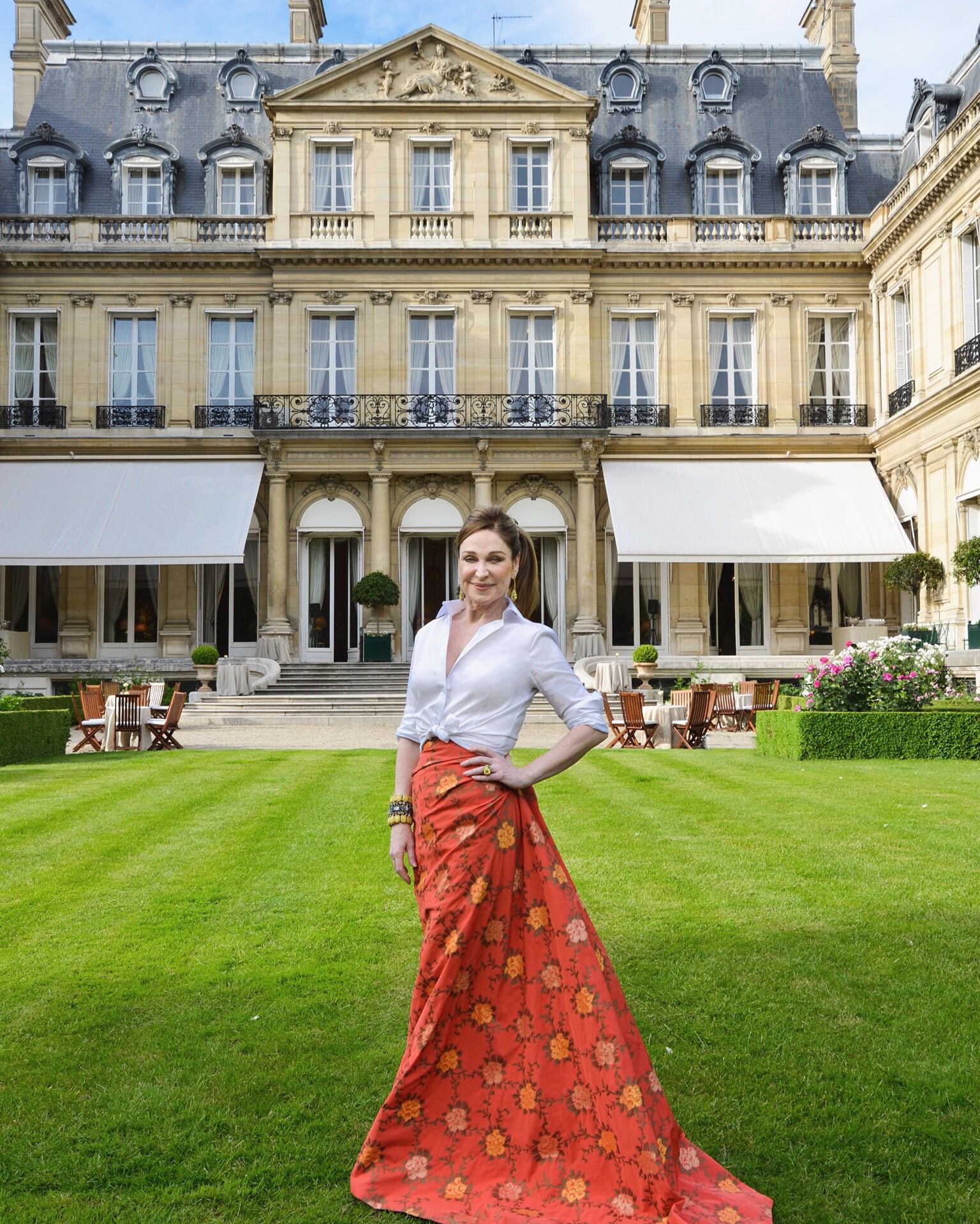 Becca Cason Thrash, a philanthropist, in a custom designed red and floral gown with a tied up white button down by David Peck posing with her hand on her hip.