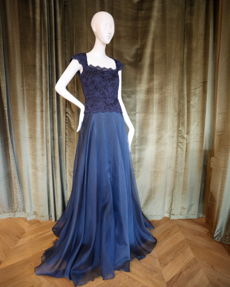 Mannequin wearing a blue evening gown with a lace top against a draped fabric background designed by David Peck