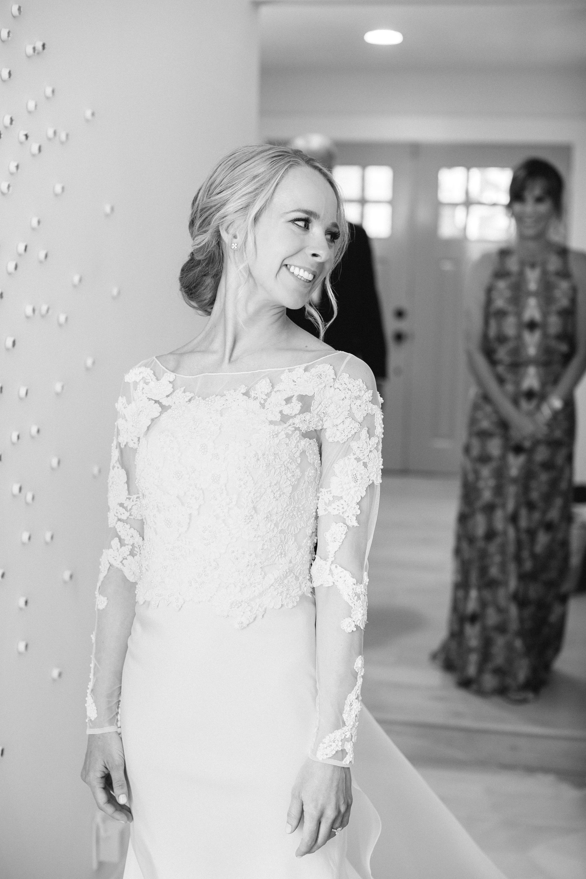 Christina Fondren Thurmond, a bride in her custom lace, floral embroidered, and long sleeve wedding gown by David Peck, smiling and looking off to the side at her wedding