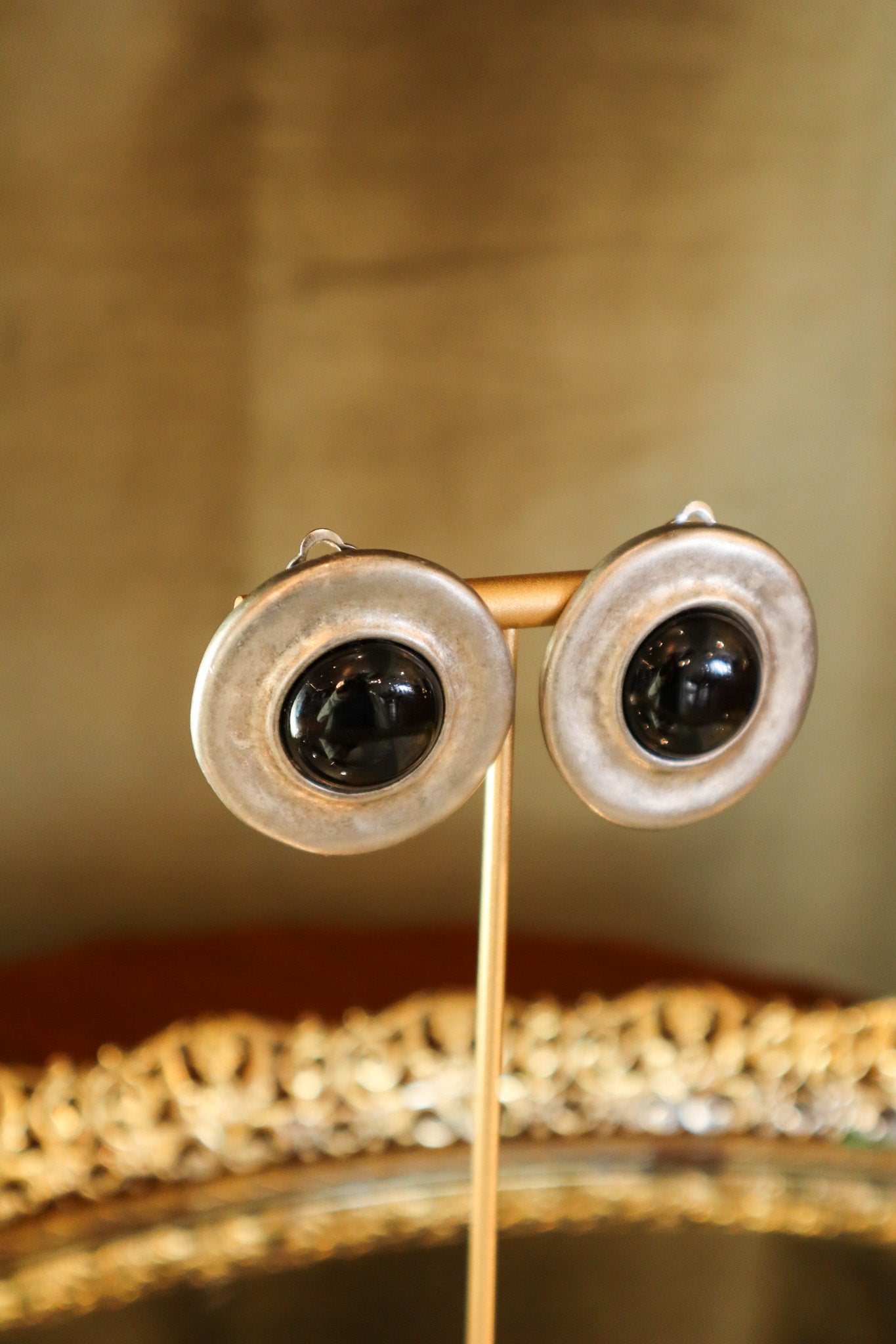 Pair of gold earrings on a stand with a reflective surface and decorative background