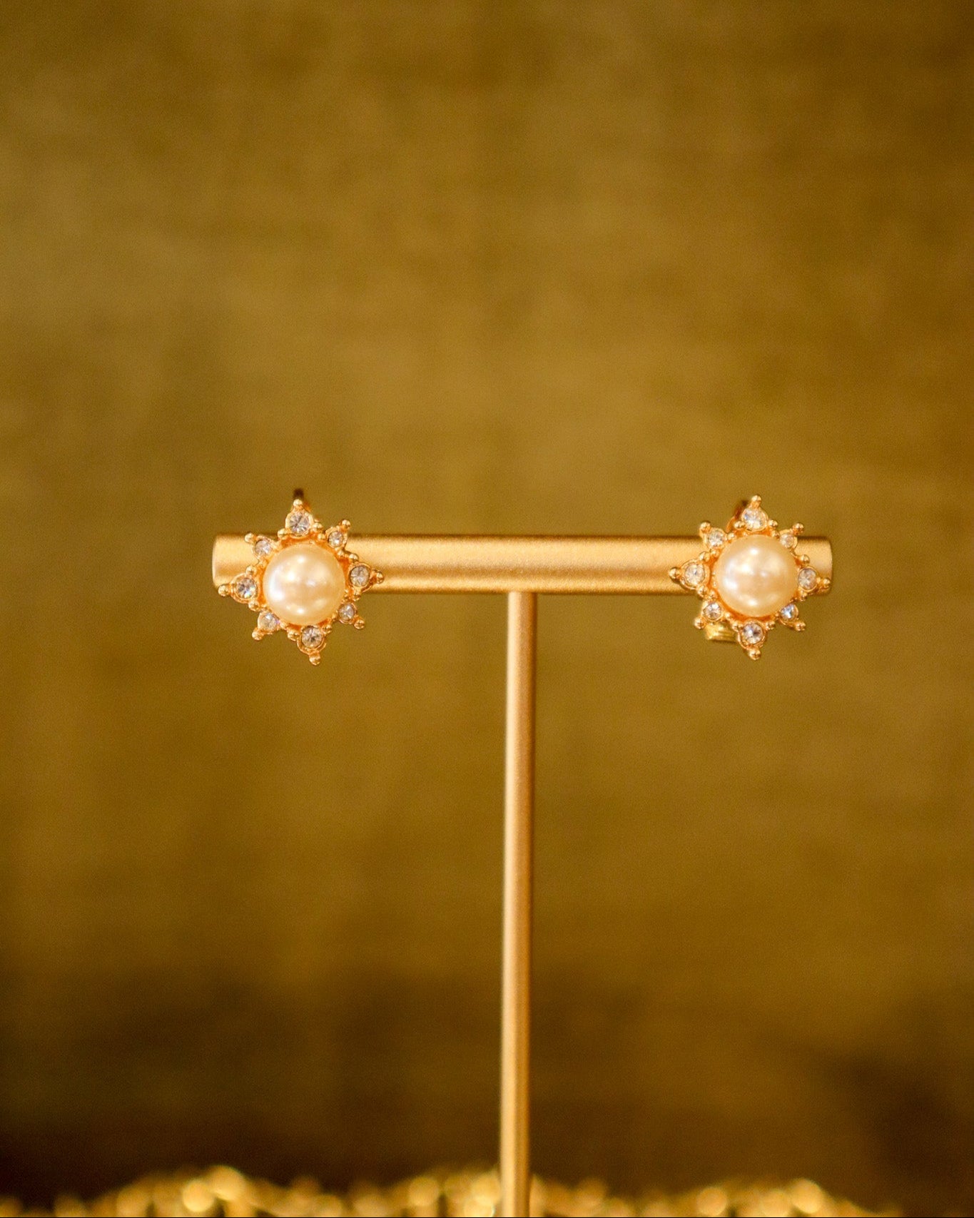 Gold earrings with pearl-like centers on a gold stand against a matching background