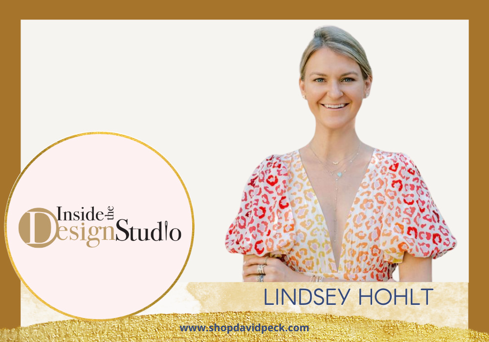 inside the design studio. Lindsey hohlt of LLJ standing with diamond bracelets, necklaces, and earrings on wearing an orange, red and yellow animal print dress.
