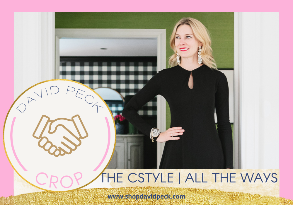 CROP. Blonde woman in black dress standing with hand on hip in doorway.