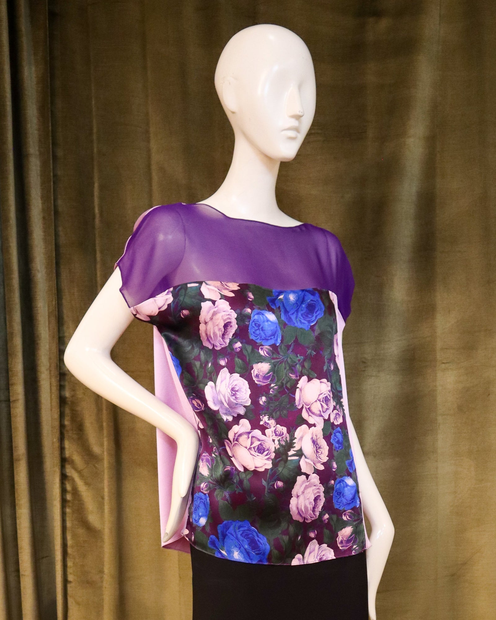 Mannequin wearing a floral top and black skirt against a olive curtain background. Designed by David Peck