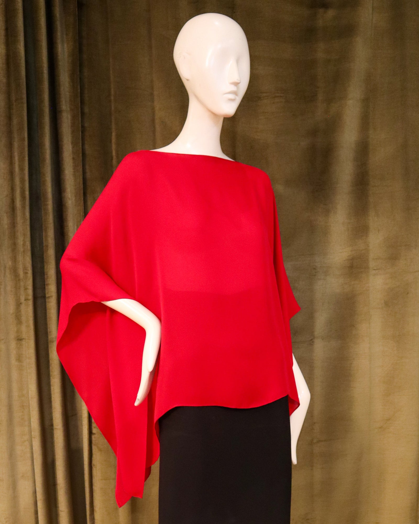 Mannequin wearing a red poncho and black skirt against a brown curtain background designed by David Peck