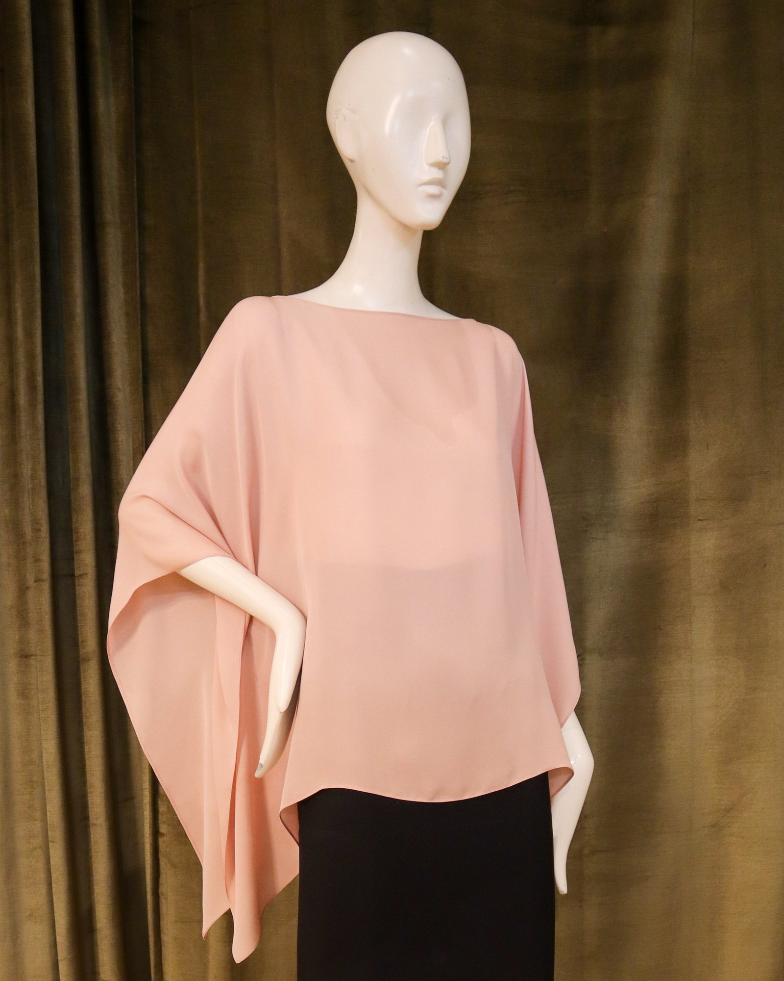 Mannequin wearing a red poncho and black skirt against a brown curtain background designed by David Peck