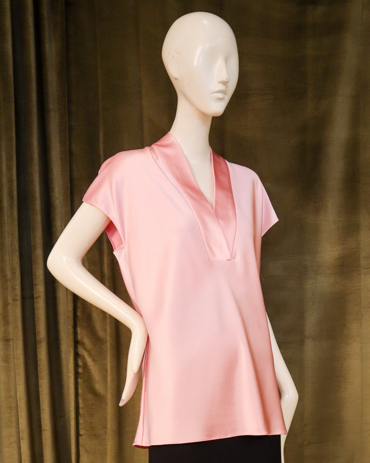 Mannequin wearing a pink top and black skirt against a green curtain. Designed by David Peck.