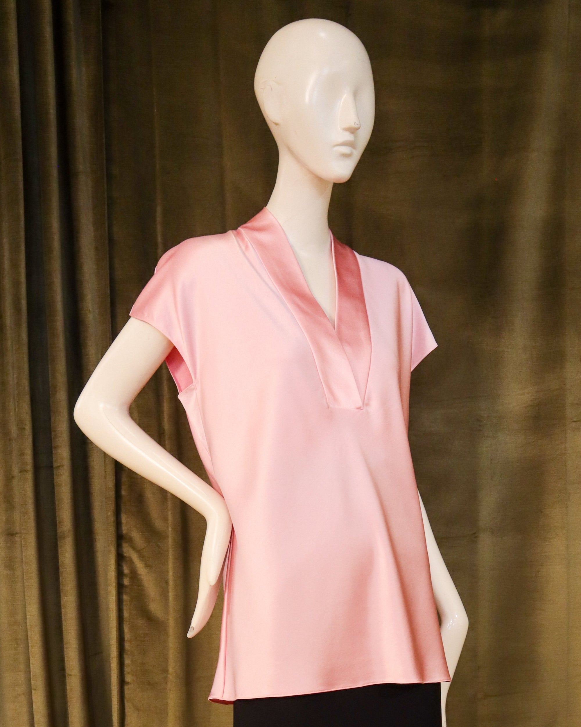 Mannequin wearing a pink top and black skirt against a green curtain. Designed by David Peck.