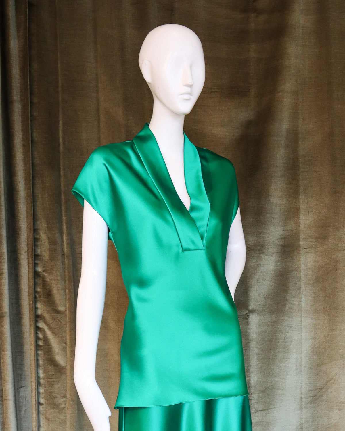 Mannequin wearing a green dress against a brown curtain background