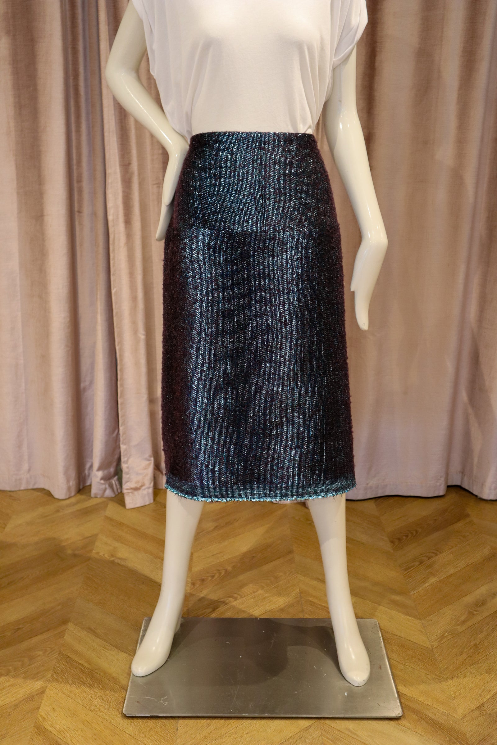 A dark navy blue tweed skirt displayed on a white mannequin, paired with a white sleeveless top, set against a backdrop of mauve curtains and a wooden parquet floor.
