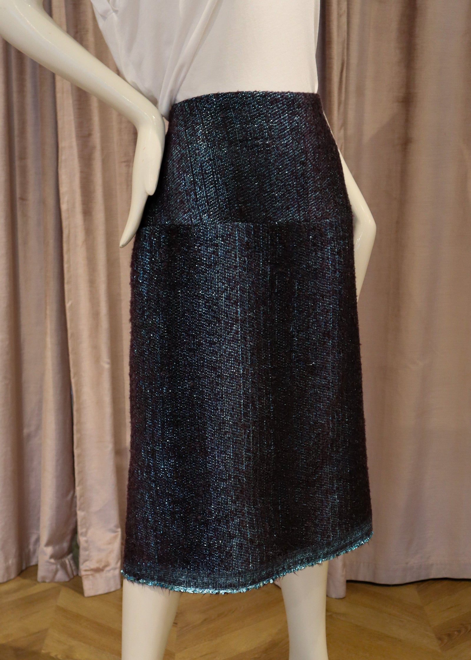 A dark navy blue tweed skirt displayed on a white mannequin, paired with a white sleeveless top, set against a backdrop of mauve curtains and a wooden parquet floor.