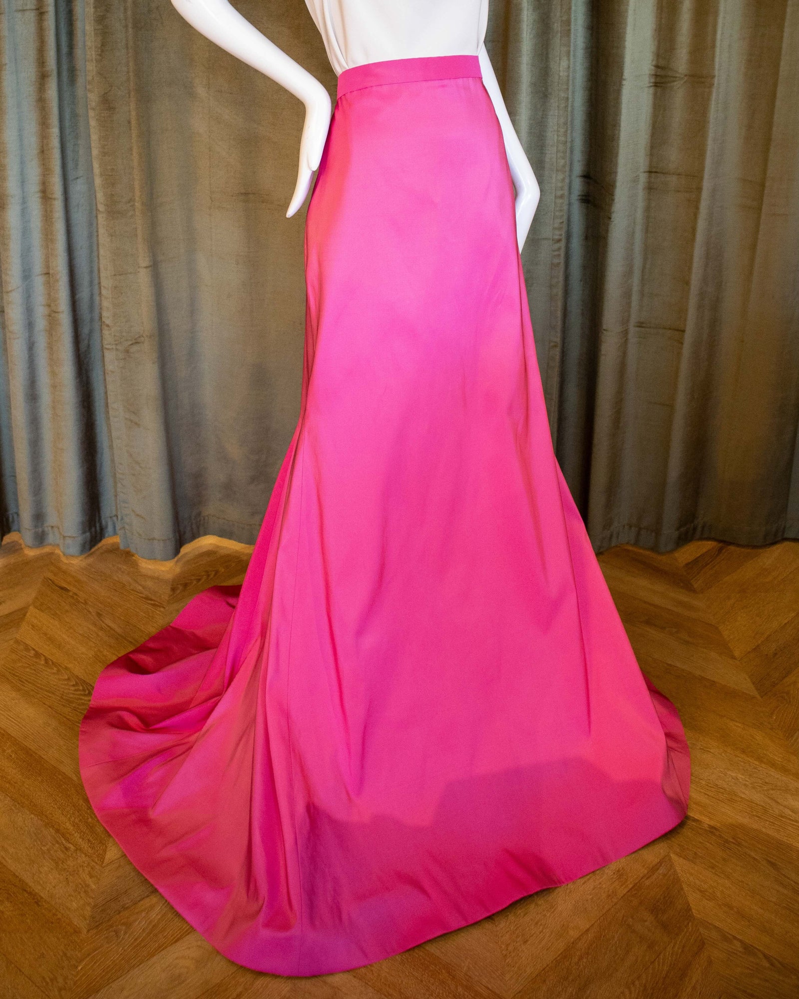 A mannequin displaying a pink silk faille skirt with a tailored fit and a dramatic sweep train. Designed by David Peck