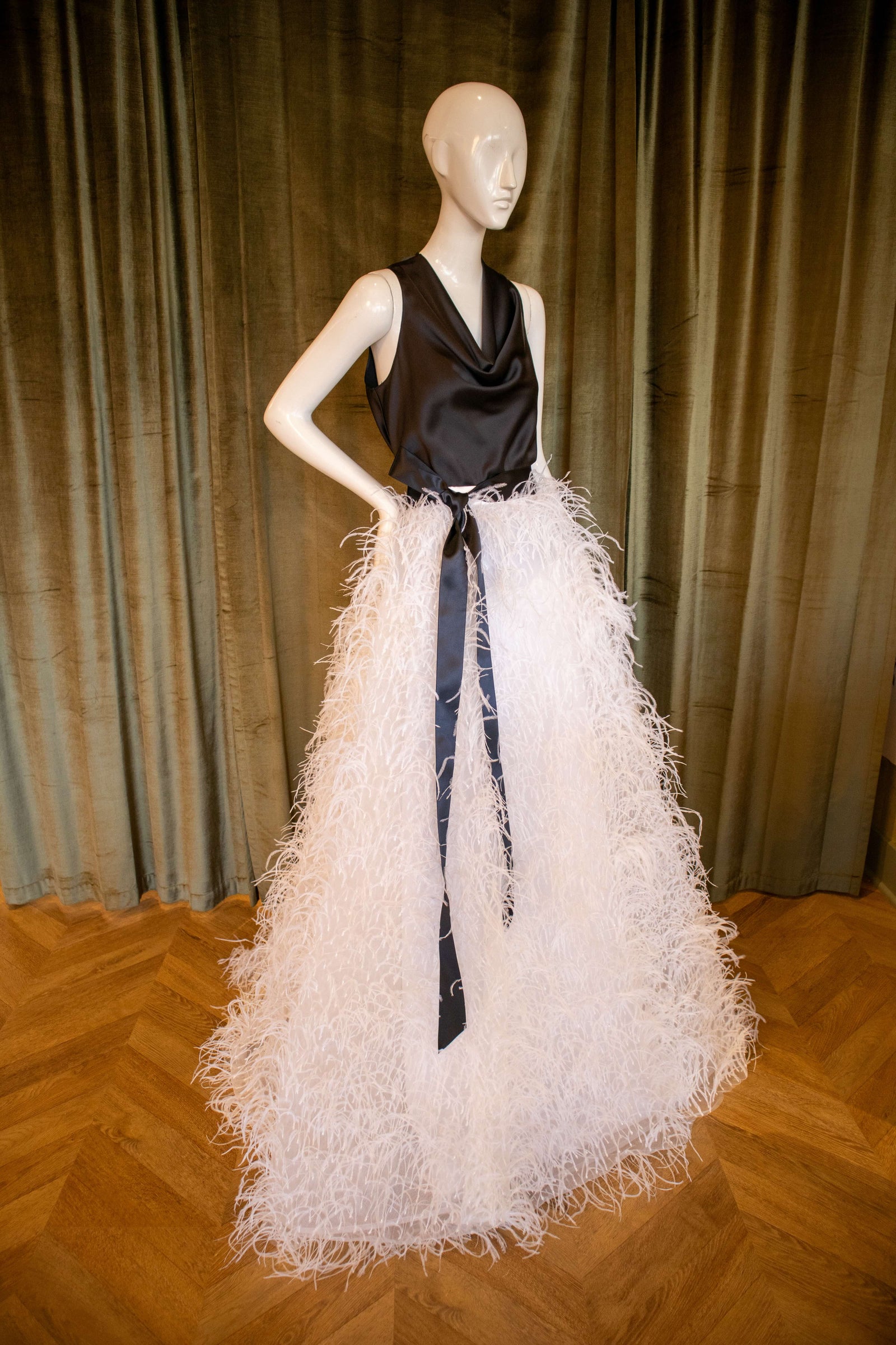 A mannequin displaying a white ostrich feather skirt with glass bead embroidery and a black top. Designed by David Peck