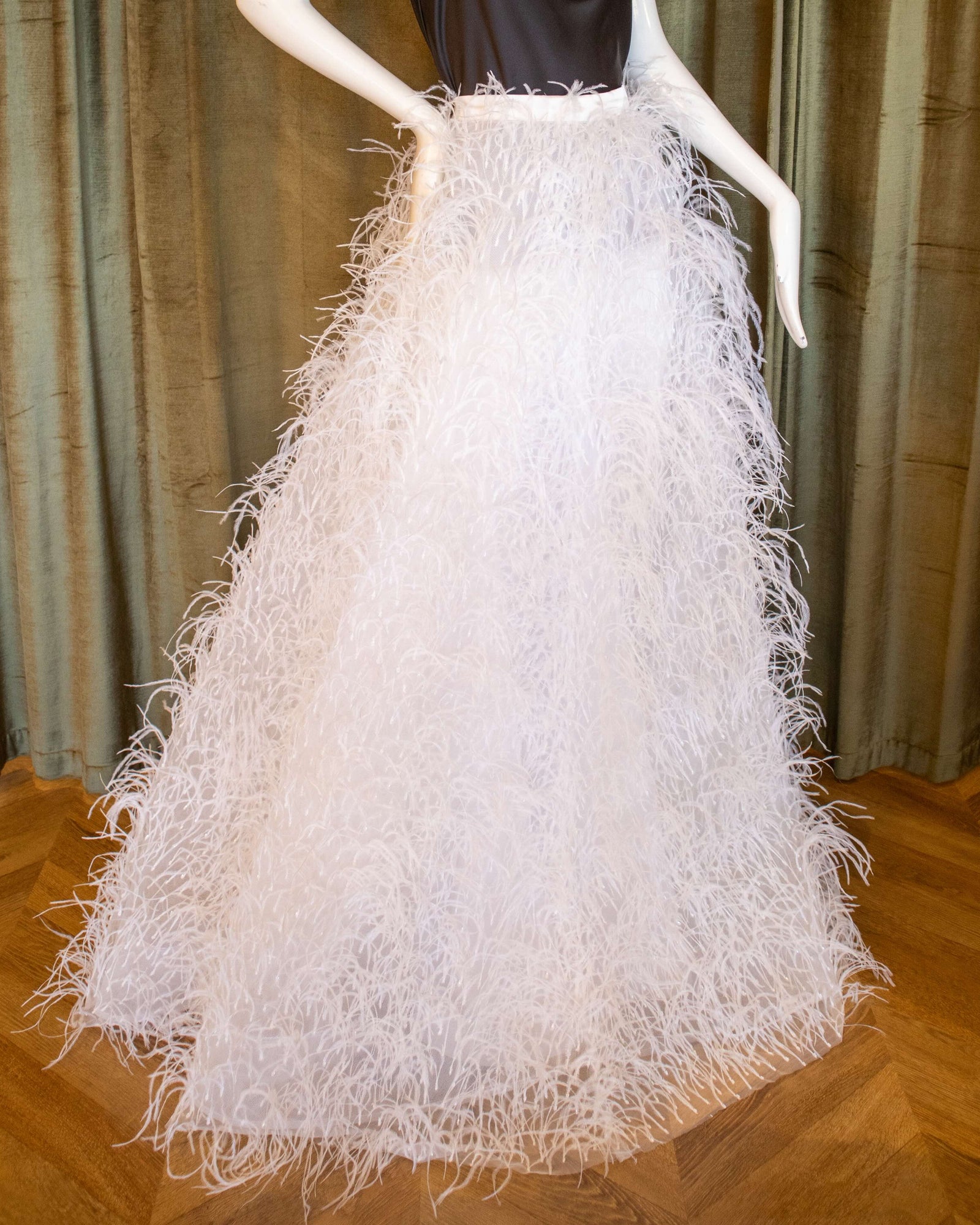 A mannequin displaying a white ostrich feather skirt with glass bead embroidery and a black top. Designed by David Peck