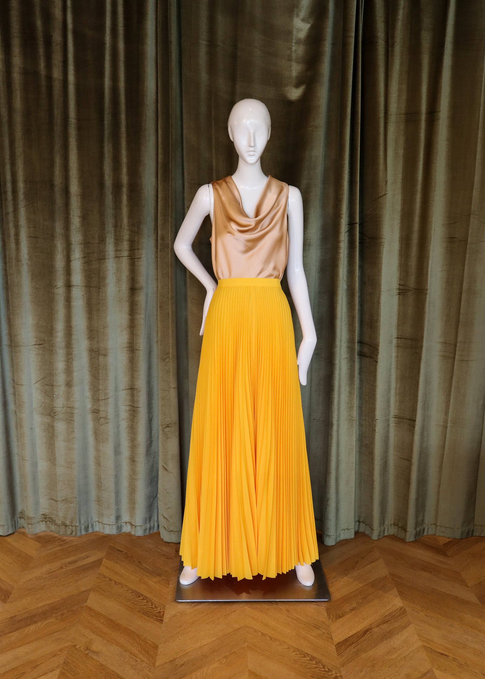 Mannequin wearing a gold top and yellow skirt against a curtain backdrop designed by David peck