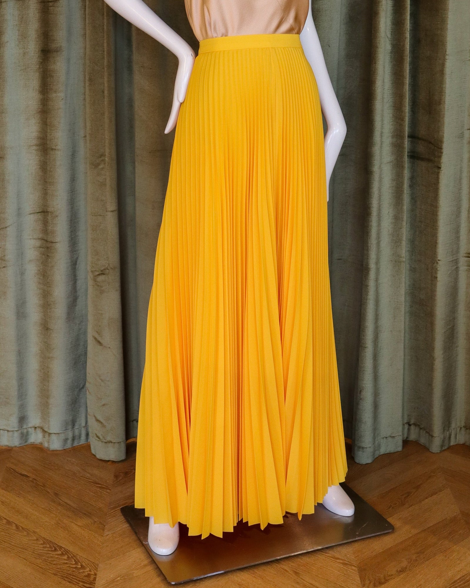 Mannequin wearing a gold top and yellow skirt against a curtain backdrop designed by David peck