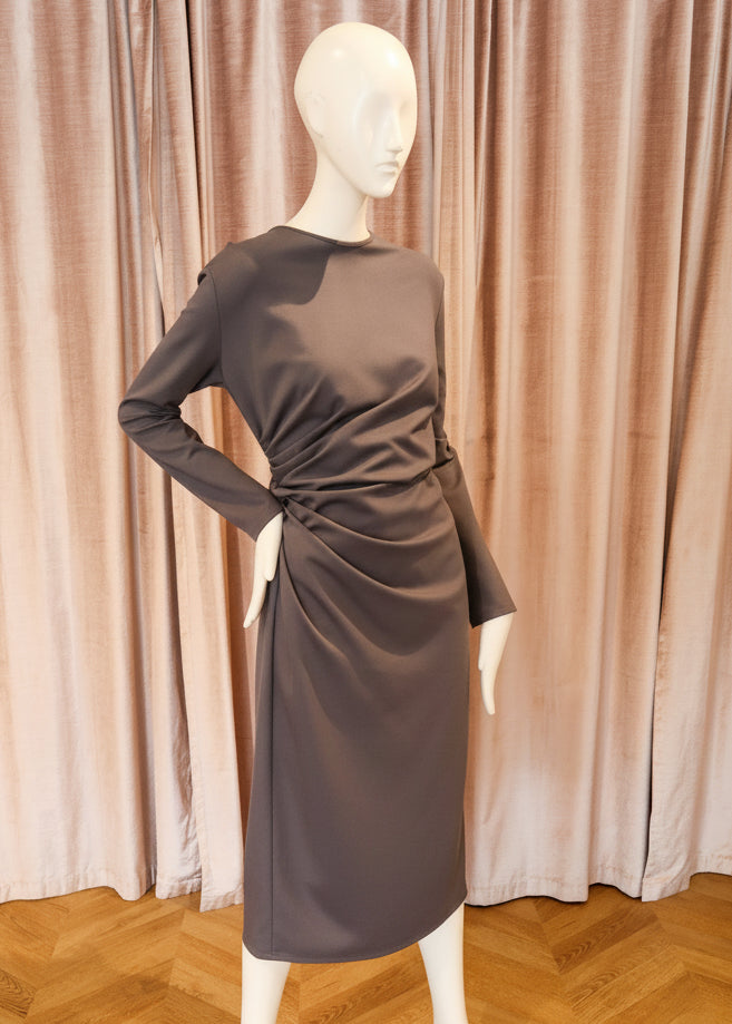 A dark graylong-sleeve dress displayed on a white mannequin, set against a backdrop of pinkish-beige velvet curtains and a light wood herringbone floor.