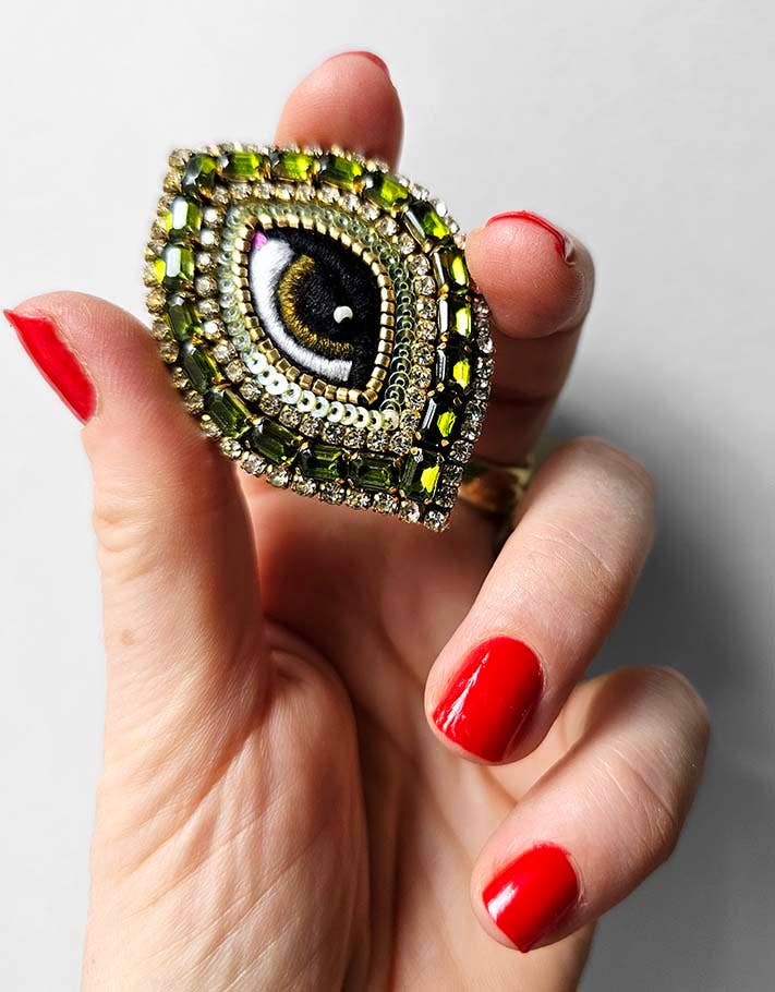 Hand holding a decorative ring with an eye design against a white background