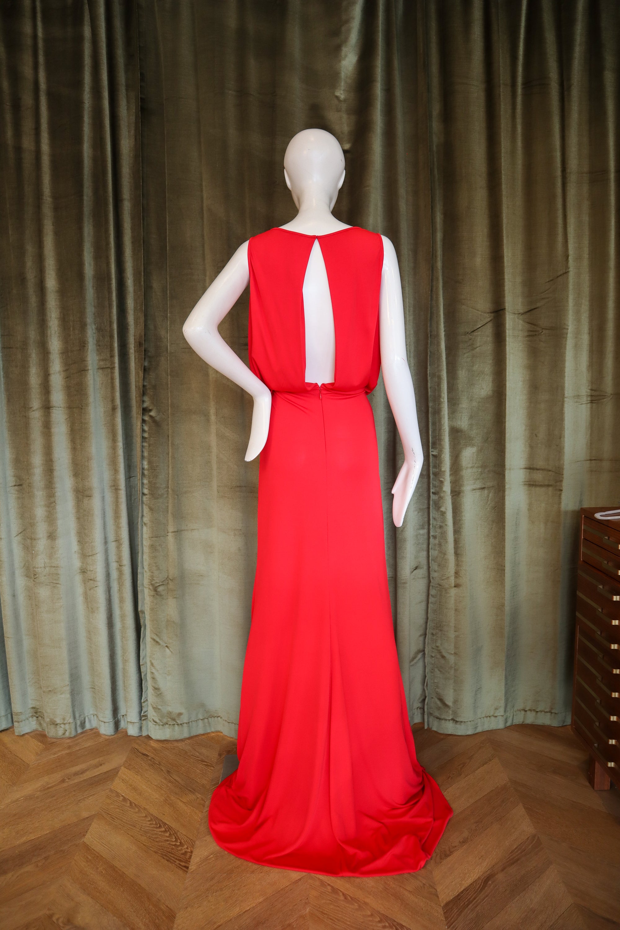 Red evening gown on a mannequin against a textured curtain background