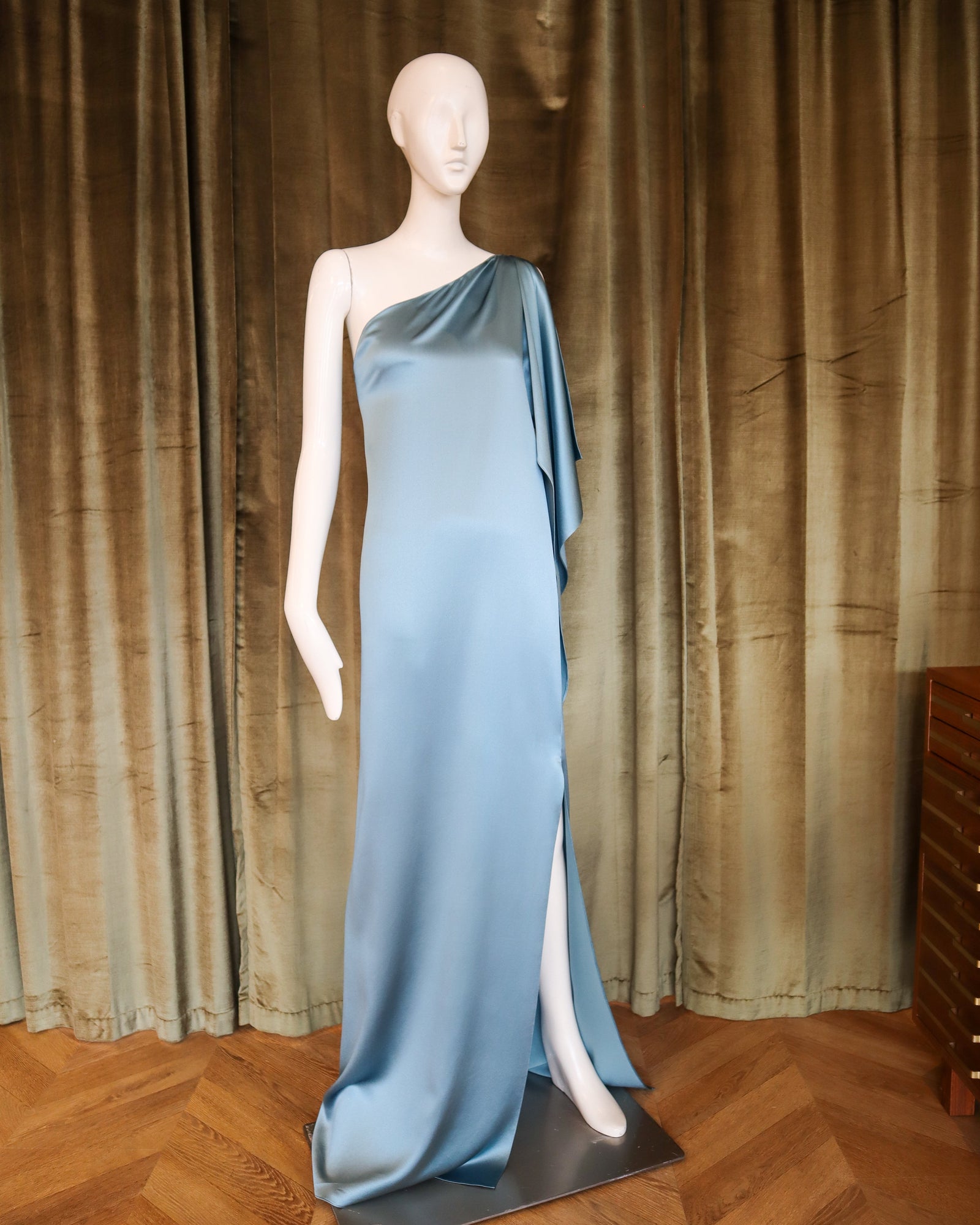 Mannequin wearing a blue evening gown against a green curtain backdrop