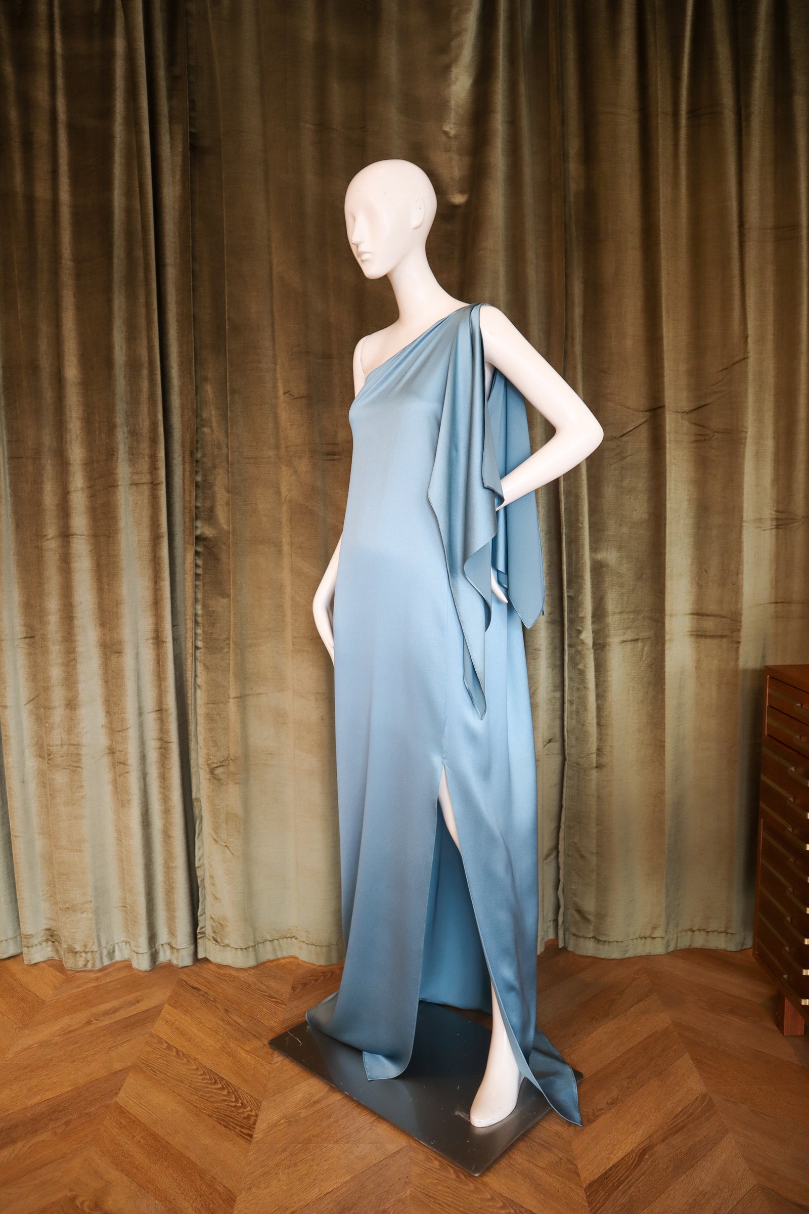 Mannequin wearing a blue evening gown against a green curtain backdrop