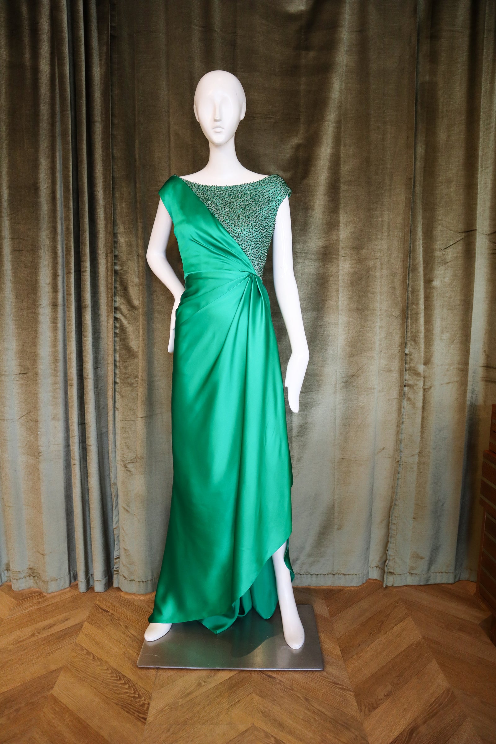 Mannequin wearing a green evening gown with a textured background