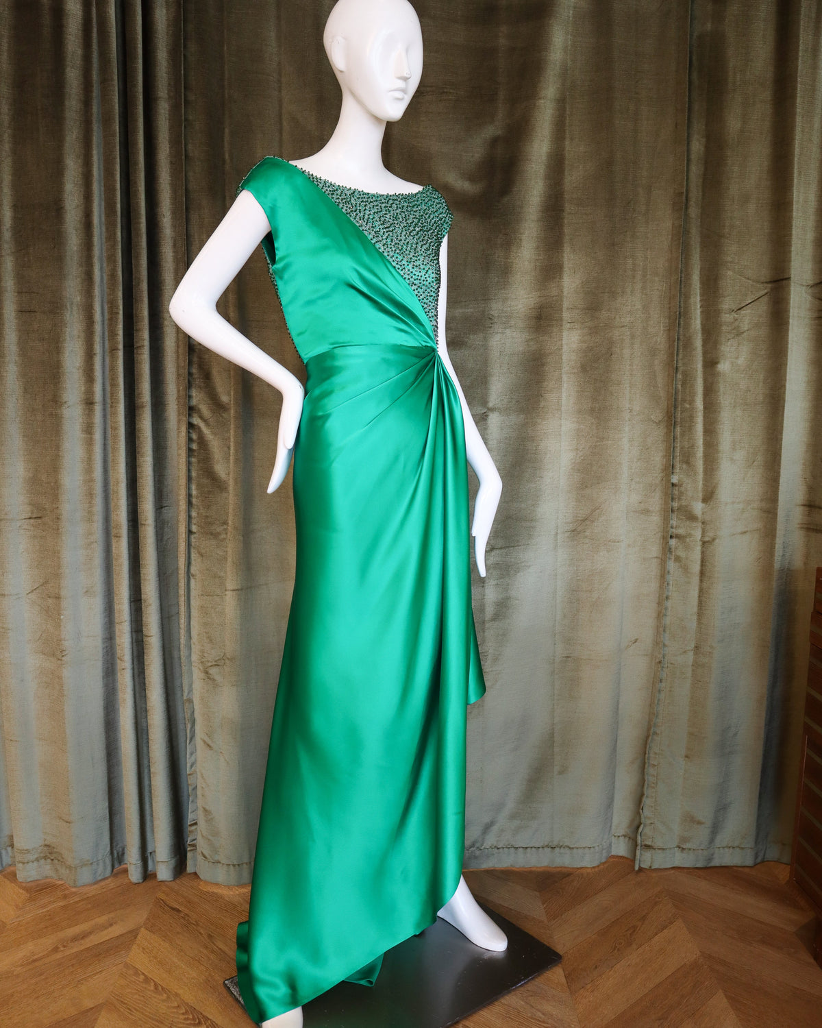 Mannequin wearing a green evening gown with a textured top against a brown curtain background