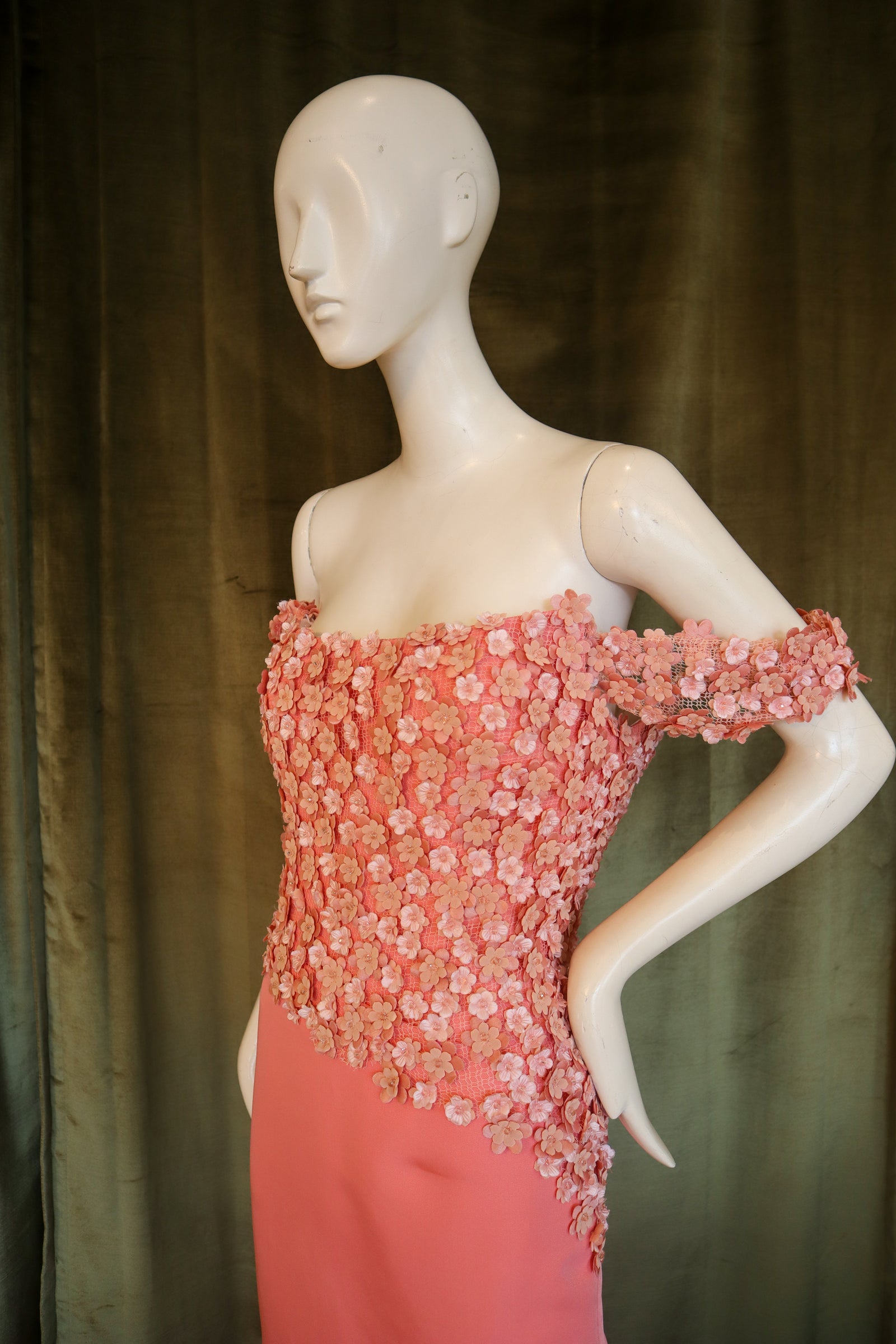 Mannequin wearing a pink evening gown with a textured bodice against a green curtain.