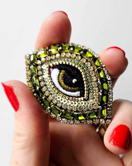 Hand holding a decorative ring with an eye design against a white background
