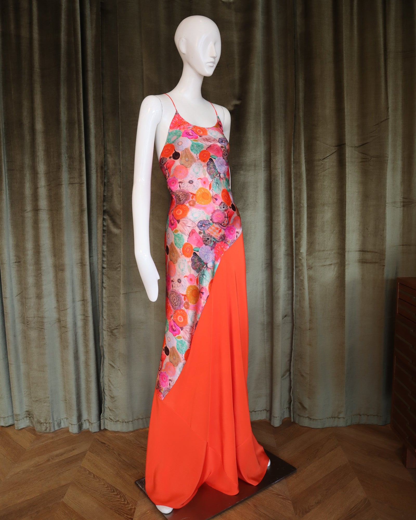 Mannequin wearing a colorful floral dress with an orange skirt on a wooden floor.