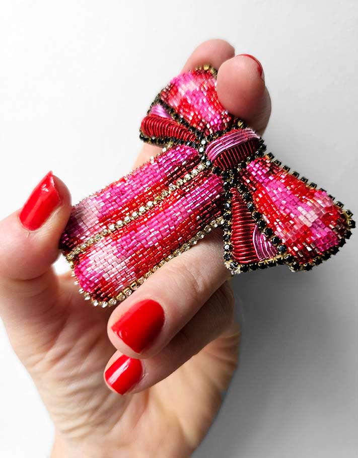 Hand holding a beaded pink and red bow against a white background