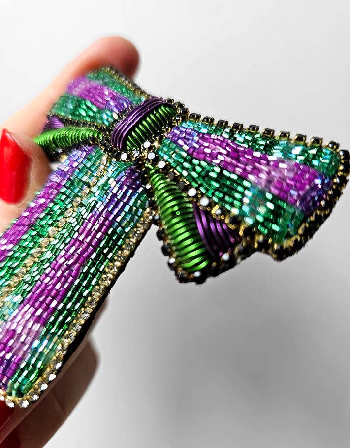 Colorful beaded bow held by a hand with red nail polish on a white background