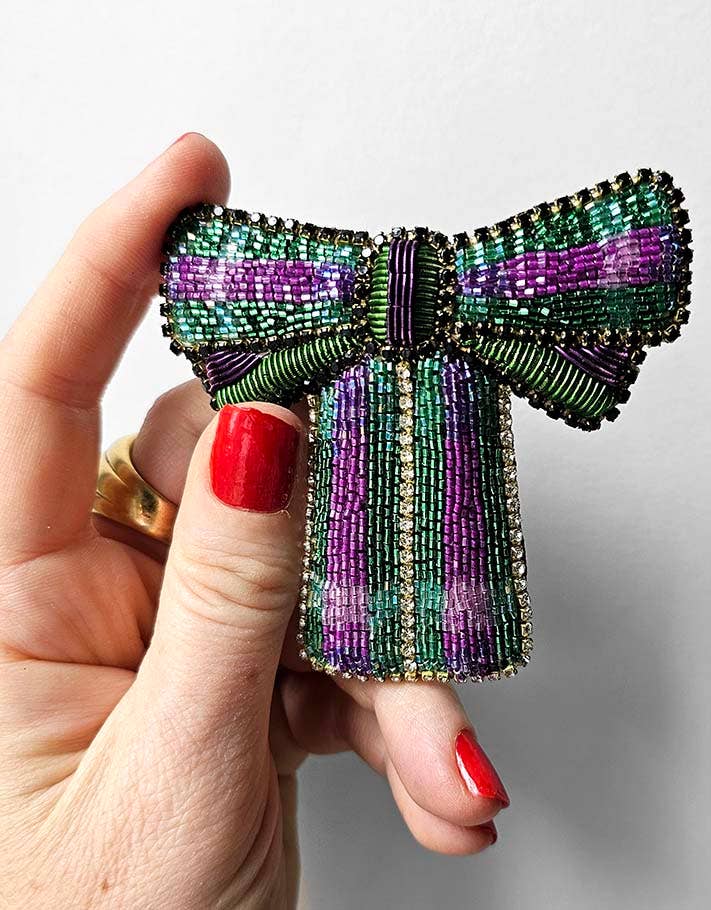 Hand holding a beaded bow-shaped jewelry piece against a neutral background