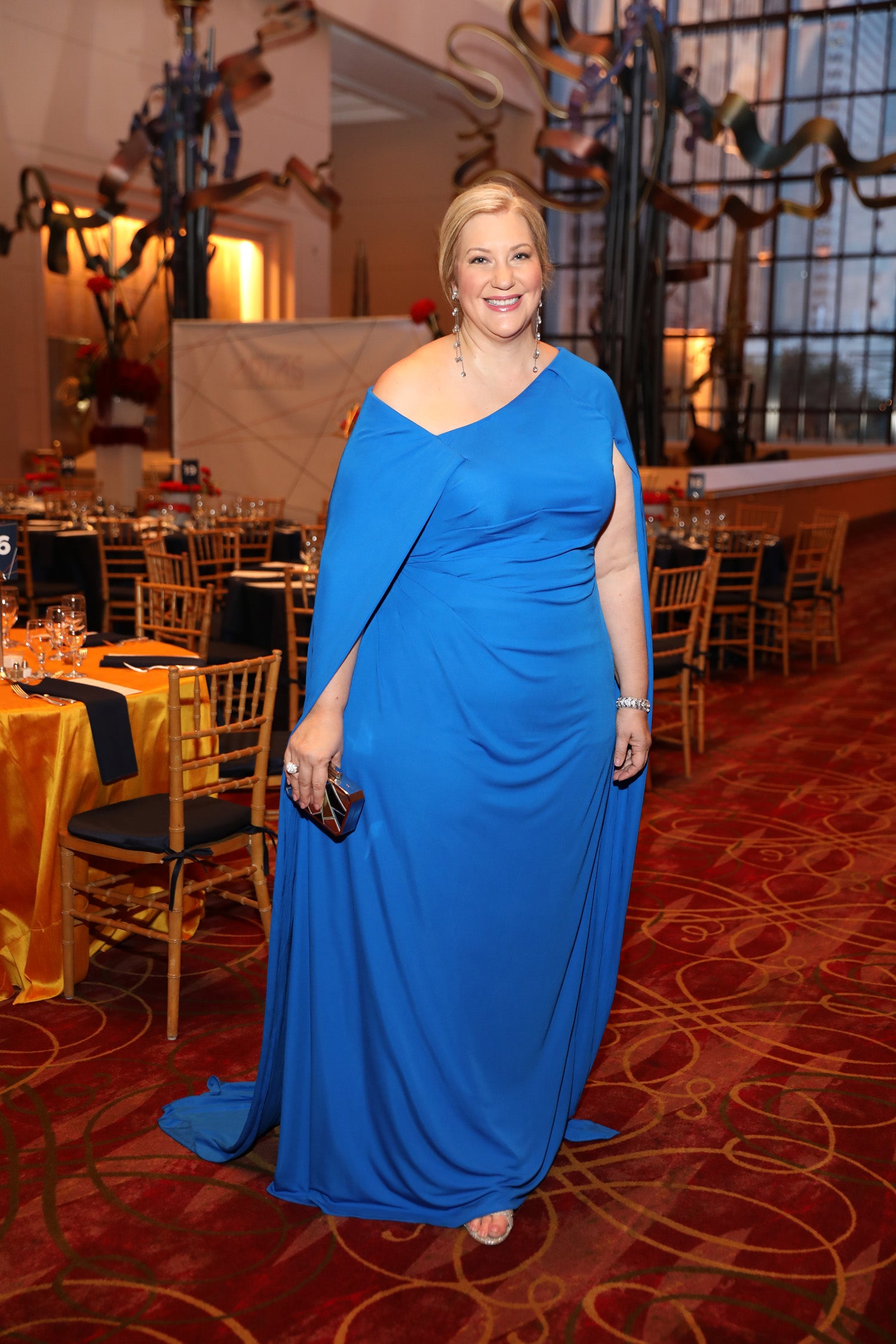 Caroline Looke Benak, a bride in her custom designed blue one shoulder Texas chic rehearsal dinner gown by David Peck, posing at her venue in Houston Oaks.
