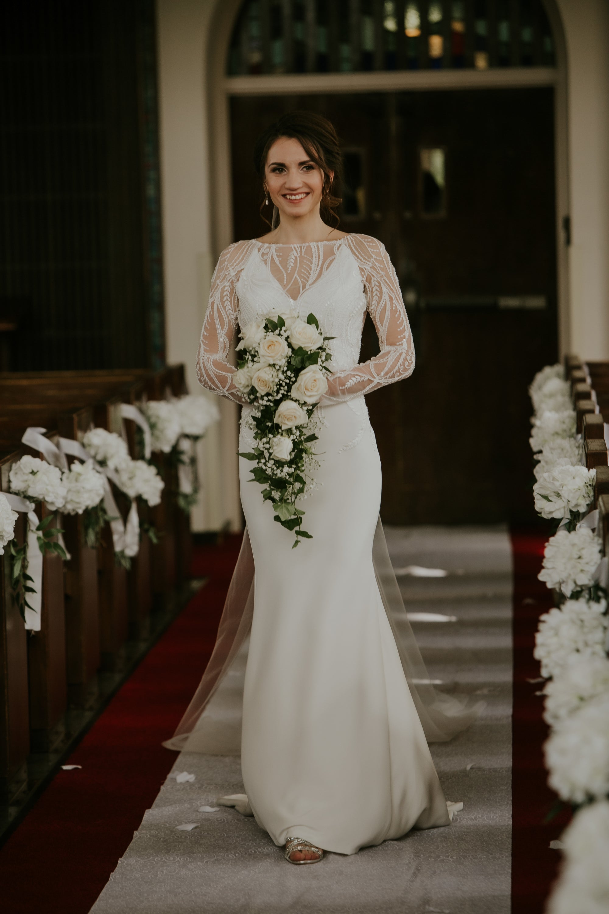 Ekaterina Moreno, a bride wearing a custom designed long sleeve mesh and silk gown by David Peck, walking down the aisle at the AD Bruce Religion Center. 