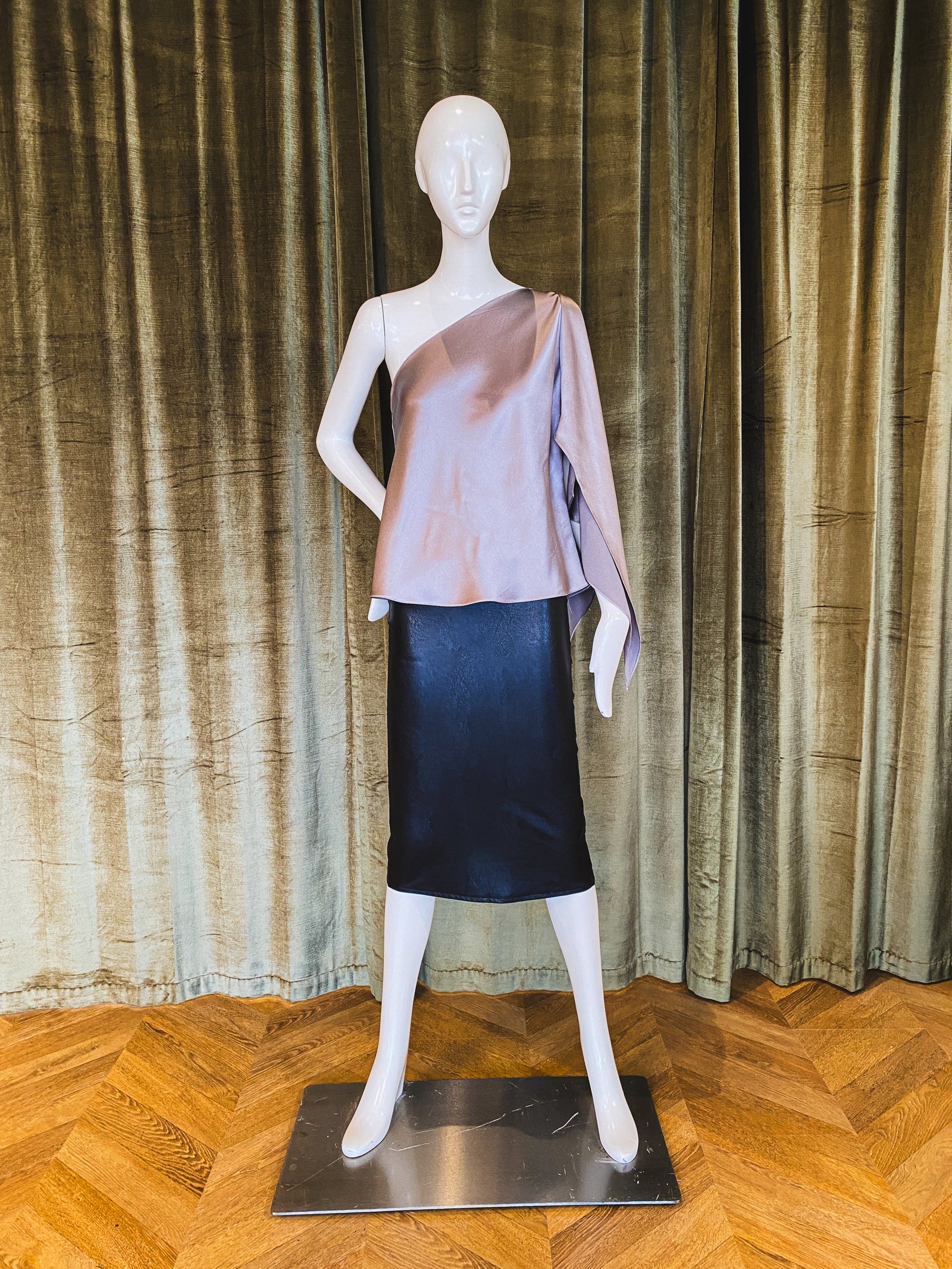 A mannequin displaying a pink one-shoulder top with scarf sleeve made of silk crepe back satin. Designed by David Peck.