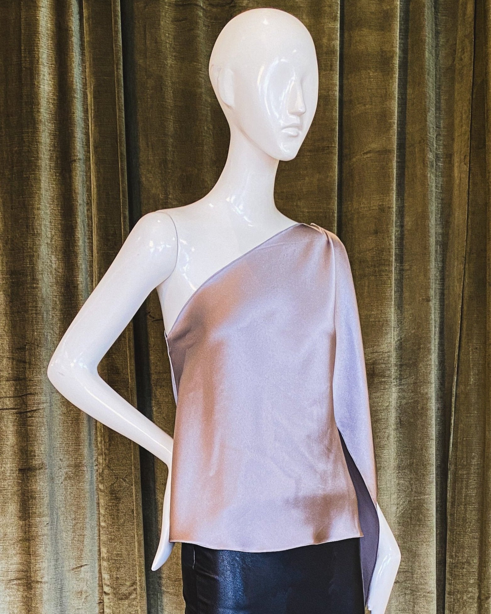 A mannequin displaying a pink one-shoulder top with scarf sleeve made of silk crepe back satin. Designed by David Peck.