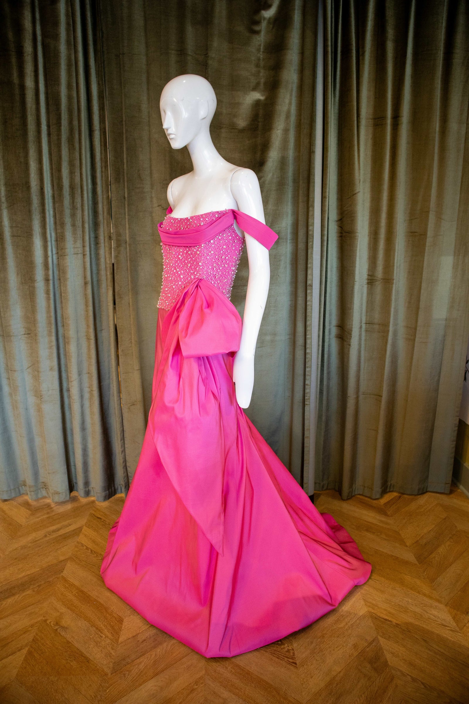 The image features a striking Barbie Bustier Top displayed on a mannequin. The top is crafted from a lustrous magenta silk faille and is detailed with an elegant crystal beading that adds a touch of glamour. Designed by David Peck