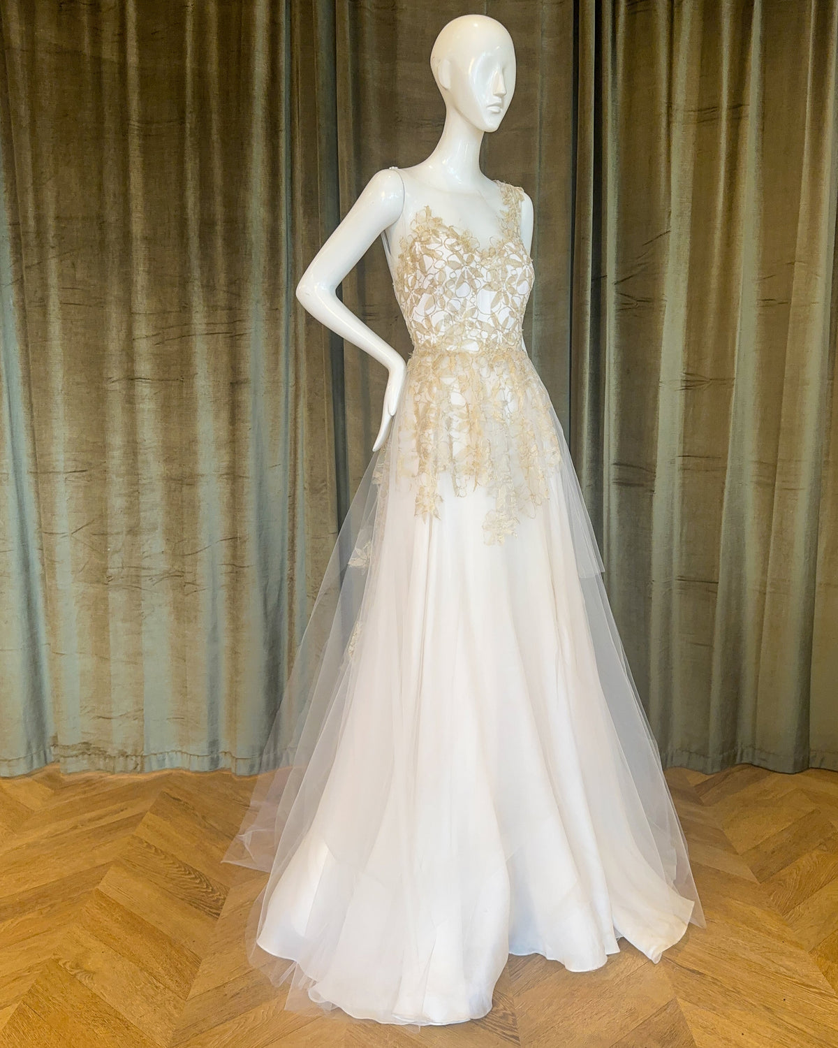 A white wedding gown with embroidered lace detailing and a full skirt, displayed on a mannequin designed by David Peck