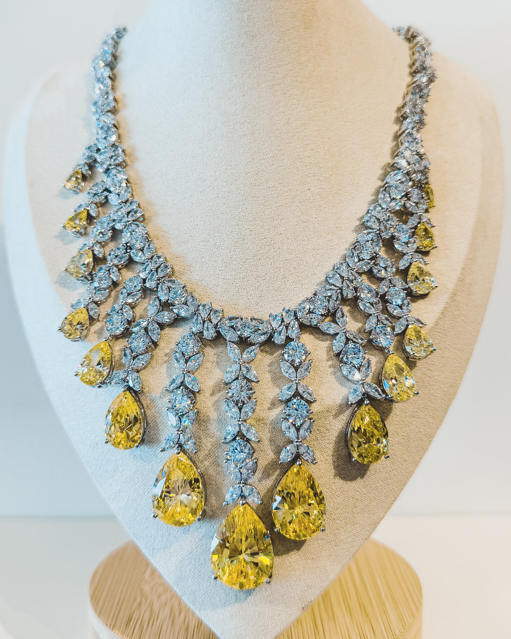 Elegant necklace with yellow and clear stones on a mannequin bust.