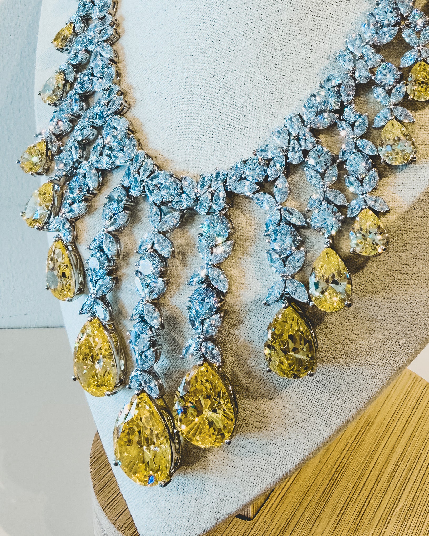 Elegant necklace with yellow and clear stones on a mannequin bust.
