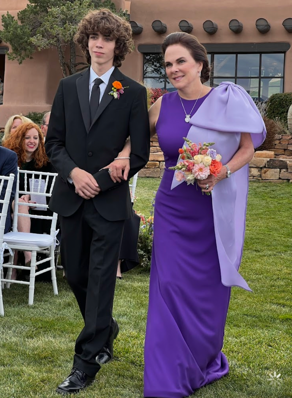 Mary Ann Detmering in her custom purple mother of the bride dress by David Peck walking down the aisle with a groomsmen